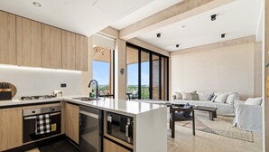 A modern kitchen with a central island, built-in appliances, and a dining area with a sofa and table. - Penthouse Unit w/ Spectacular Ocean & Golf Views (Playa del Carmen)