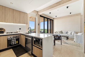 A modern kitchen with a central island, built-in appliances, and a dining area with a sofa and table. - Penthouse Unit w/ Spectacular Ocean & Golf Views (Playa del Carmen)