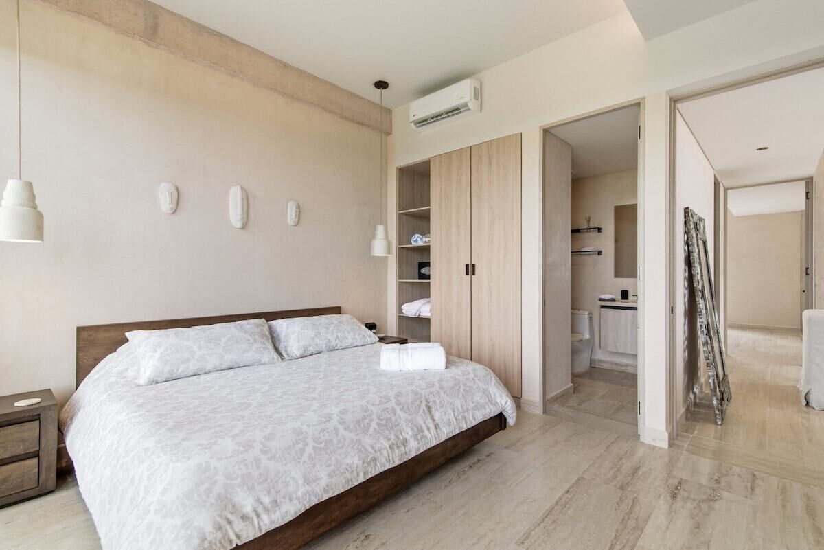 A modern bedroom with a large bed, built-in wardrobe, and a bathroom visible through an open door.