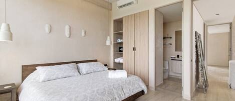 A modern bedroom with a large bed, built-in wardrobe, and a bathroom visible through an open door.