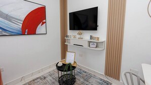 Ein modernes Wohnzimmer mit einem flachbildfernseher an der Wand über einer weißen Konsole, einem gerahmten Zertifikat auf einem kleinen Tisch und einer Zierpflanze.
