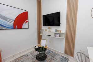 A modern living room with a flat-screen TV mounted above a white console, a framed certificate on a small table, and a decorative plant. - Modern 1BR in Plaza Clara in Bayahibe (San Rafael del Yuma)