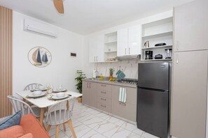 A modern kitchen with white cabinets, a stainless steel refrigerator, and a dining area with a table set for two. - Modern 1BR in Plaza Clara in Bayahibe (San Rafael del Yuma)