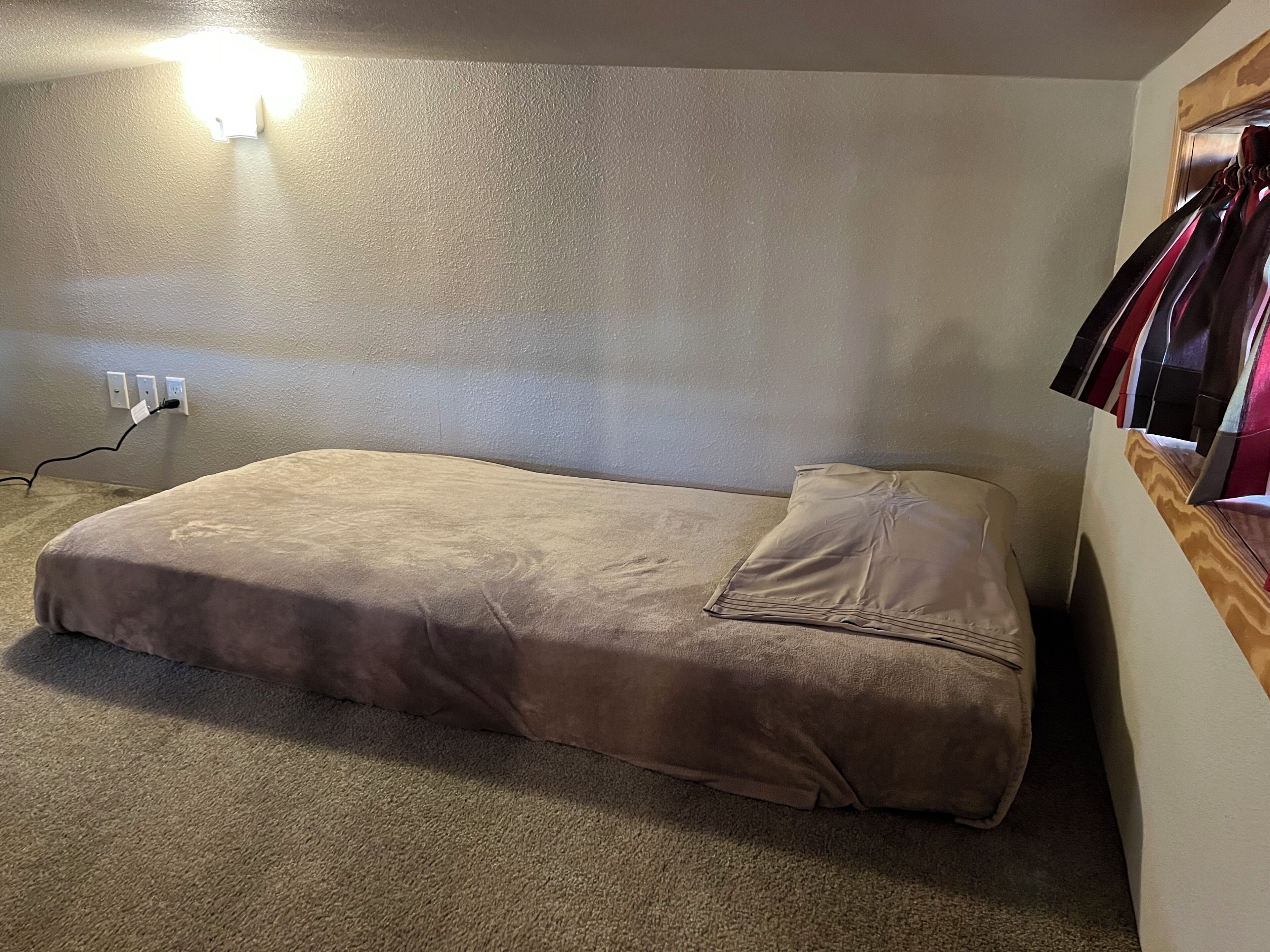 Ein Einzelbett in einem Zimmer mit Teppichboden, einer Wandleuchte und einer Steckdose.