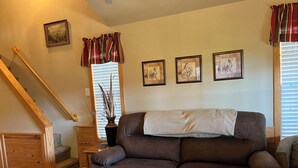 A living room with a brown leather sofa, a wooden staircase, and a window with blinds.