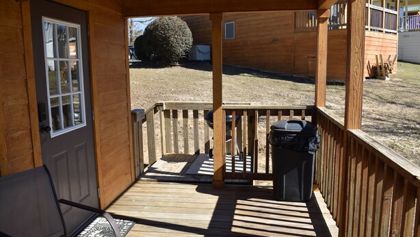 A wooden deck with a railing, a bench, and a trash can.