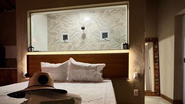 A hotel room with a large bed, a headboard with a mirror, a wall-mounted air conditioner, and a small bedside table. - OKA VIVAH - Chalet Oka das Aguas (Jaboticatubas)