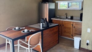 A compact kitchen with a dining area, featuring a wooden island, white chairs, and hanging pendant lights. - OKA VIVAH - Chalet Oka das Aguas (Jaboticatubas)
