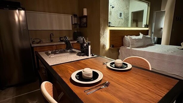 A compact kitchen with a dining table set for two, a refrigerator, and a hanging light fixture.