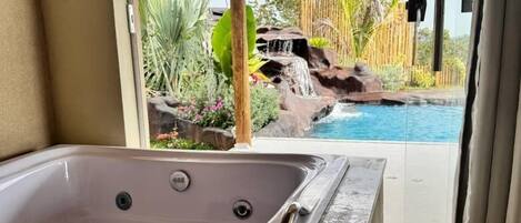 A spa area with a hot tub, a view of a waterfall, and a pool.