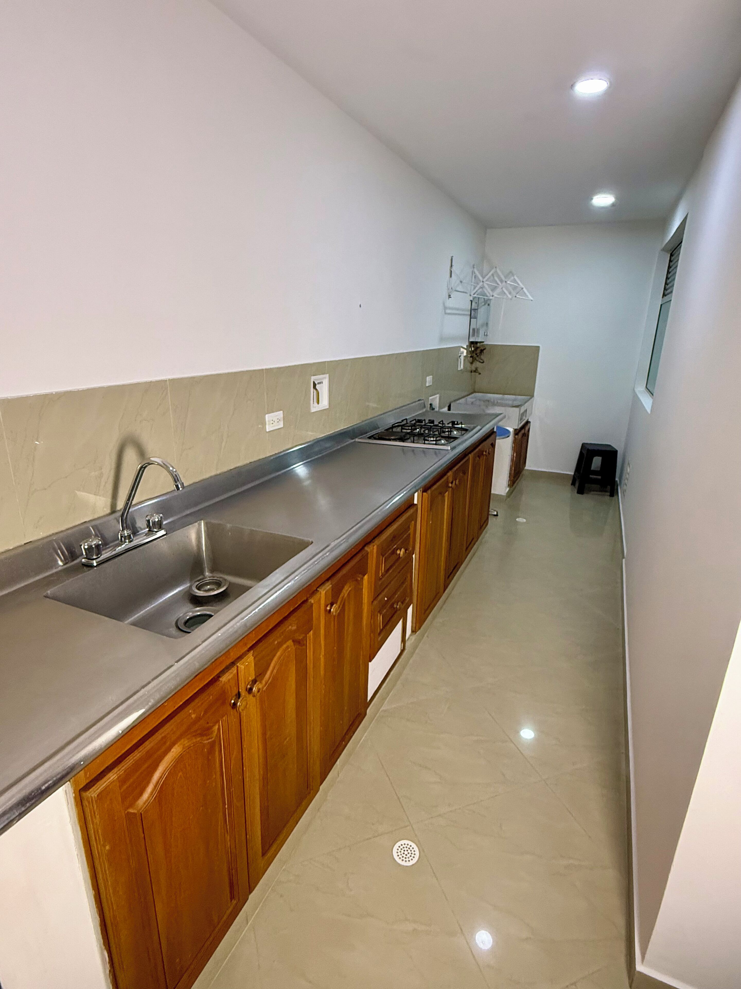 Una cocina con un lavamanos de acero inoxidable, armarios de madera y piso de baldosas.