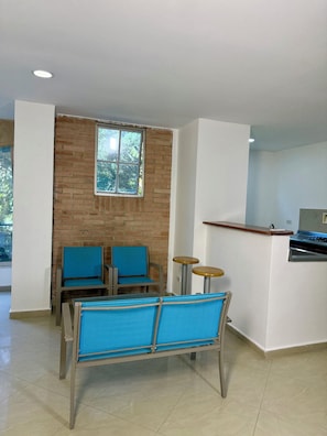 A room with a brick wall, a window, a kitchenette, and a seating area with chairs and a table. - Living Montes (MedellÃn)
