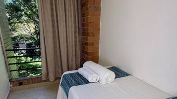 Habitación de hotel con cama, ventana con cortinas y vista a zonas verdes, además de piso de baldosas.