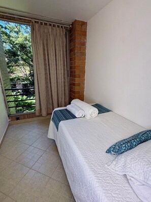 Habitación de hotel con cama, ventana con cortinas y vista a zonas verdes, además de piso de baldosas.