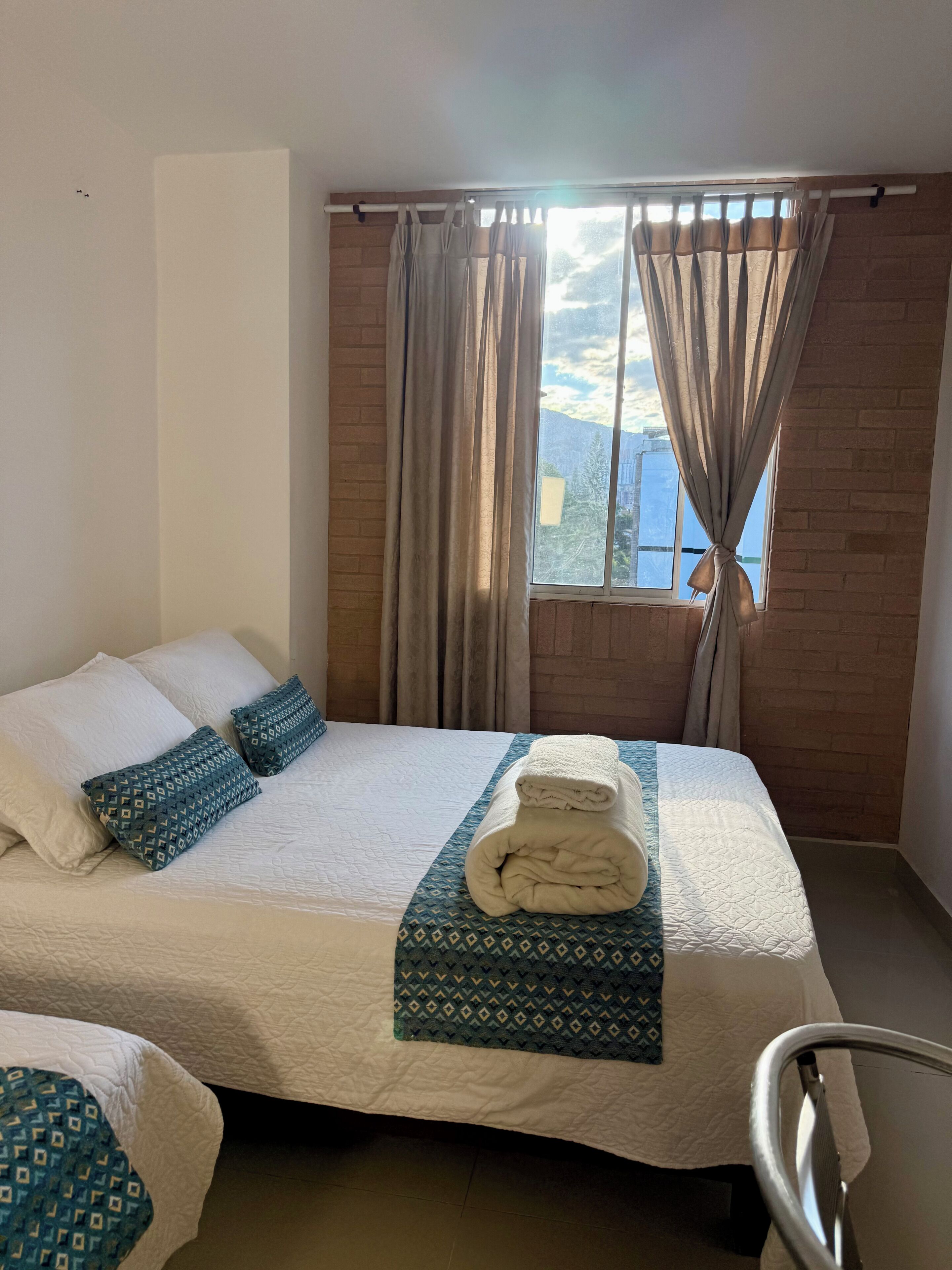 Una habitación de hotel con cama, almohadas, una colcha y cortinas.