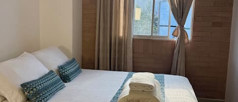 A hotel room with a bed, pillows, a blanket, and curtains.