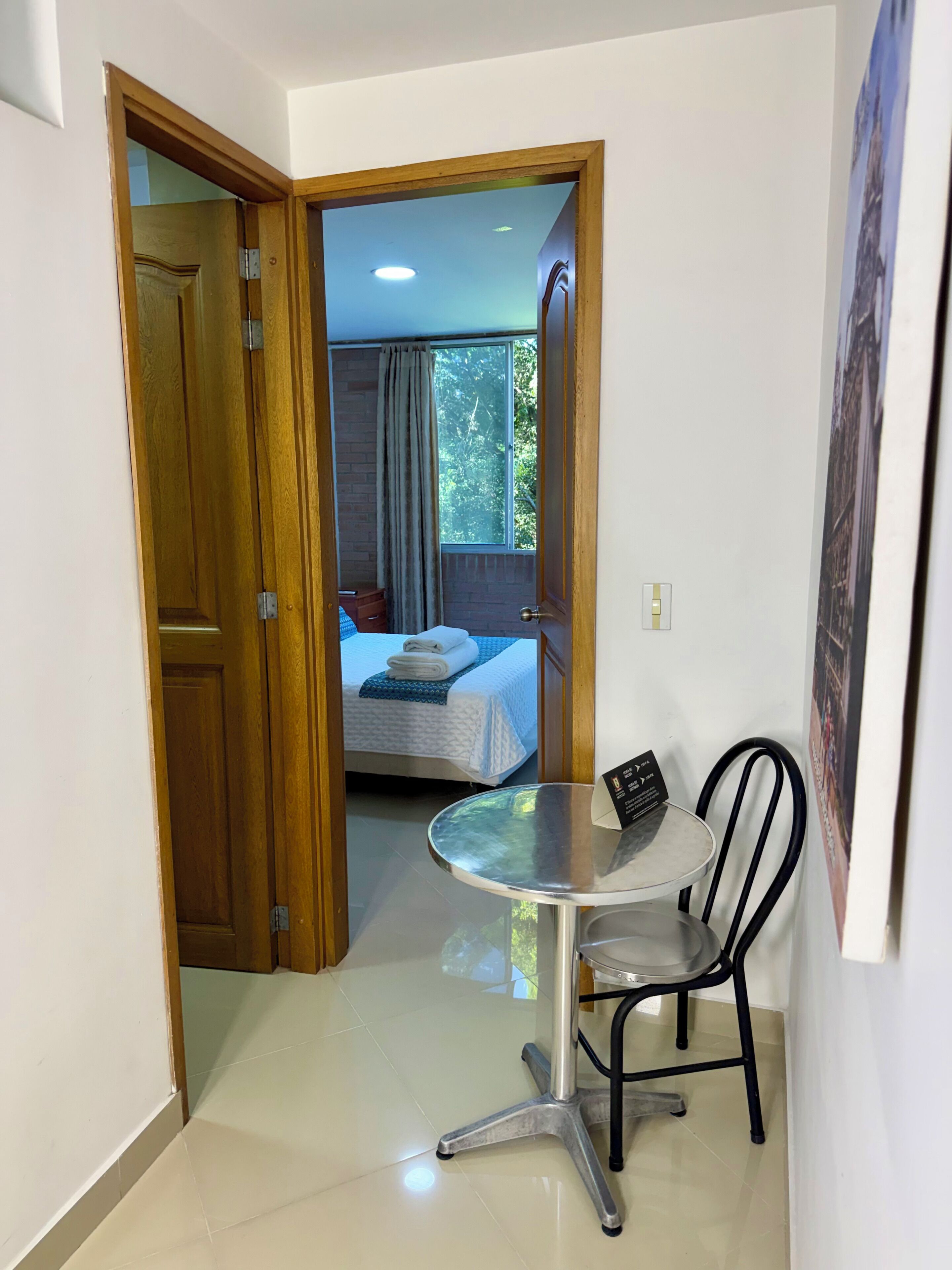 Una habitación de hotel con cama, una mesita con silla y vista al exterior por una ventana.