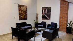 Um quarto com chão de azulejos, móveis de vime preto, duas pinturas penduradas na parede e uma parede de tijolos.