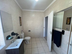 A bathroom with a toilet, sink, and mirror. - Stylish 1-bed Cottage,garden, Pool &secure Parking (Alberton)