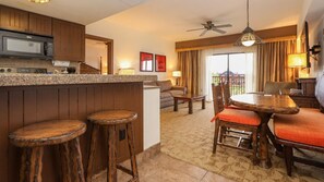A kitchen with wooden cabinets, a microwave, and a bar area with stools. There is a dining table with chairs and a ceiling fan. - Orlando | Couples Safari Retreat | Pool + Hot Tub (Kissimmee)