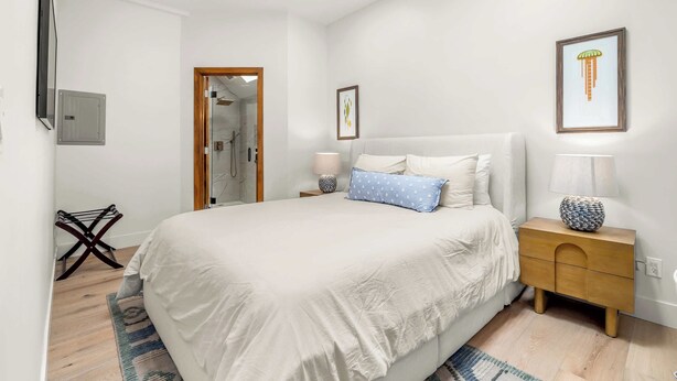 A bedroom with a bed, bedside tables, a nightstand, a mirror, and a door leading to a bathroom. - Luxury Capitola Retreat | Hot Tub | Blocks to Sand (Capitola)