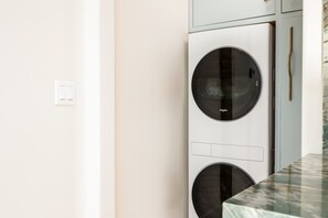 A modern kitchen with a built-in Whirlpool washer and dryer, a marble countertop, and a light-colored wall. - Luxury Capitola Retreat | Hot Tub | Blocks to Sand (Capitola)