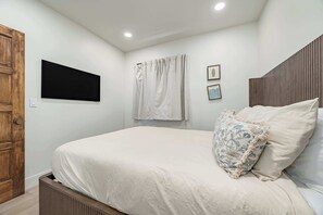 Ein Schlafzimmer mit einem Bett, einer Holztür, einem Flachbildfernseher und zwei gerahmten Bildern an der Wand.