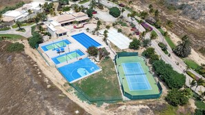Eine Vogelperspektive zeigt eine Wohngegend mit mehreren Tennisplätzen, einem Schwimmbad und umliegender Grünfläche.
