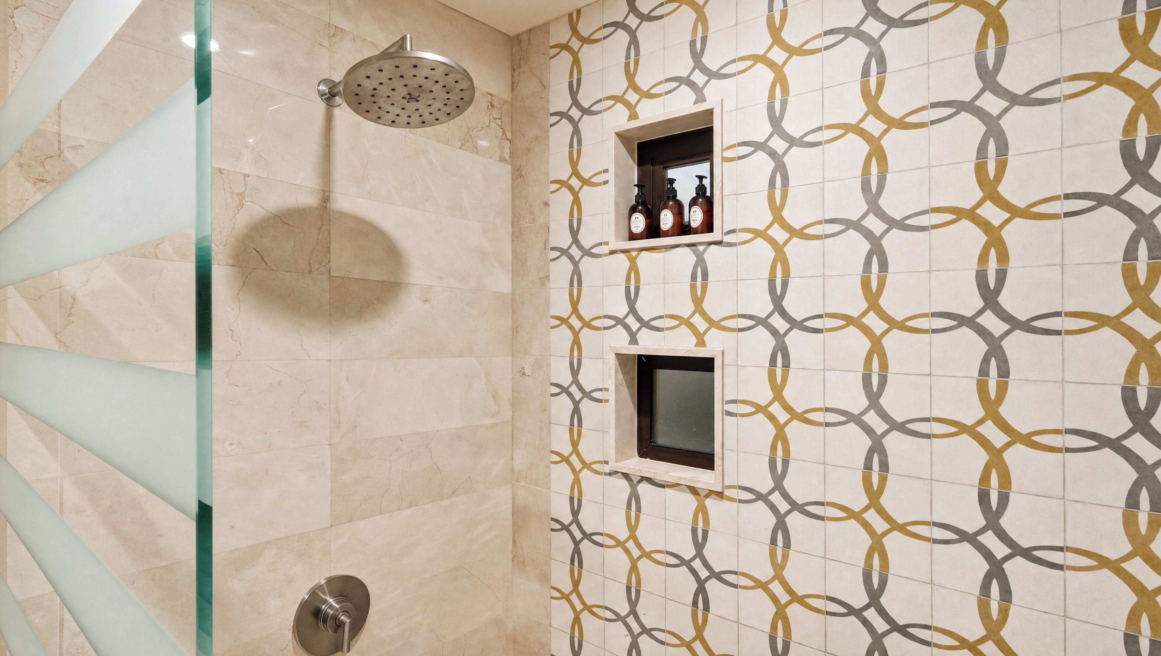 A bathroom with a shower, a glass partition, and a tiled wall with a geometric pattern.
