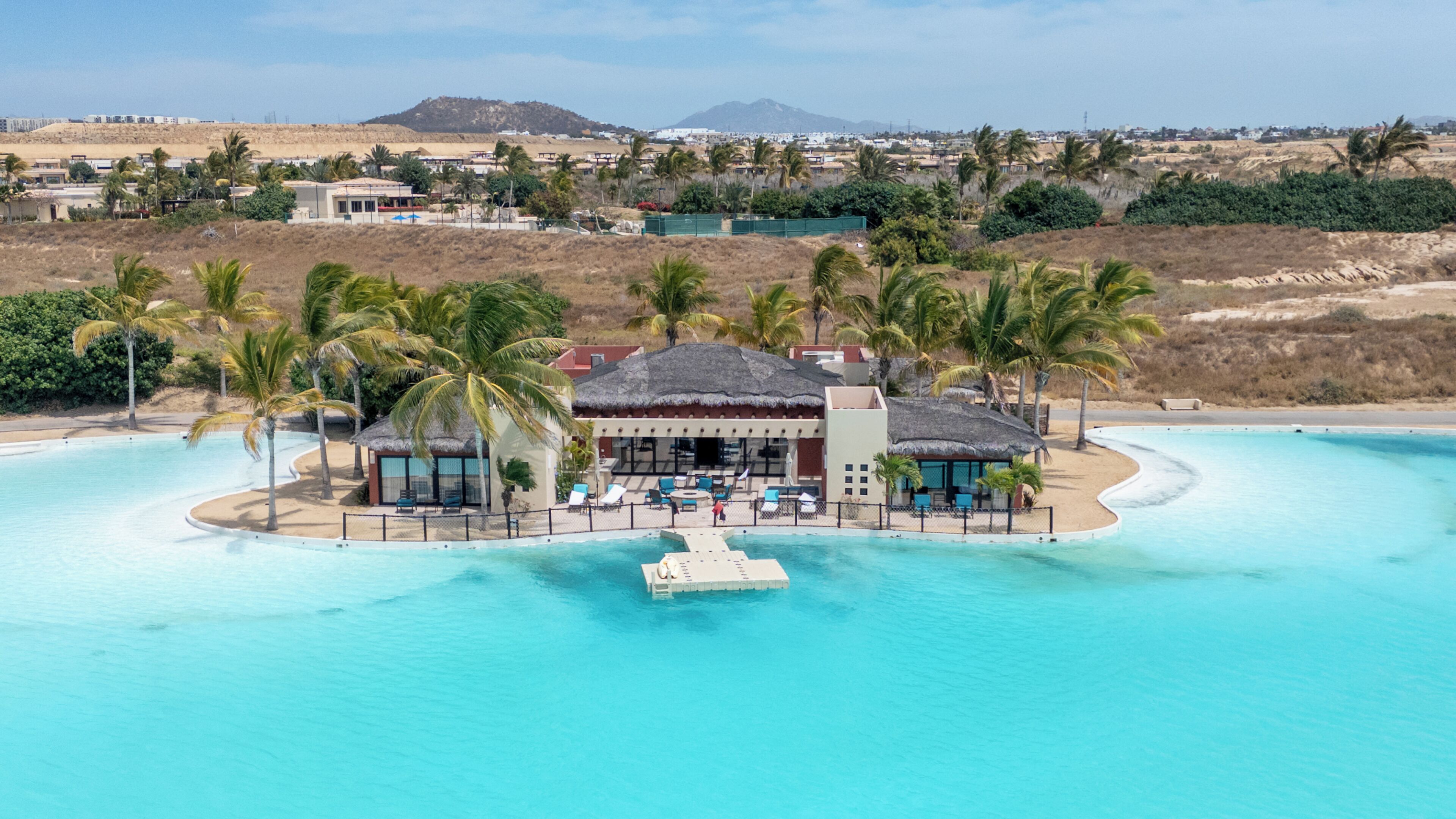 Ein Resort mit Pool, Palmen und einem Gebäude mit einem Reetdach.