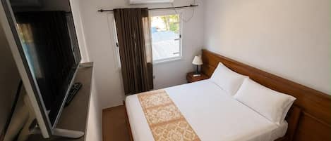 A hotel room with a bed, a TV, an air conditioning unit, and a window with curtains.