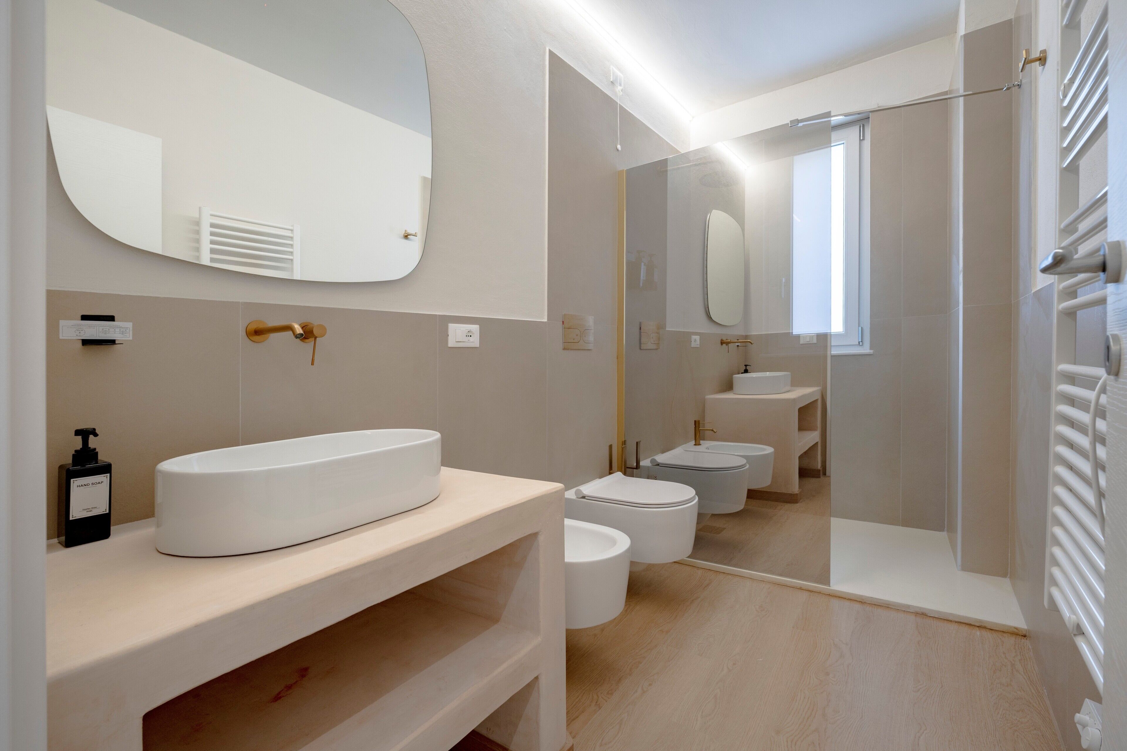 A modern bathroom with a large oval sink, a mirror, a toilet, and a shower area.