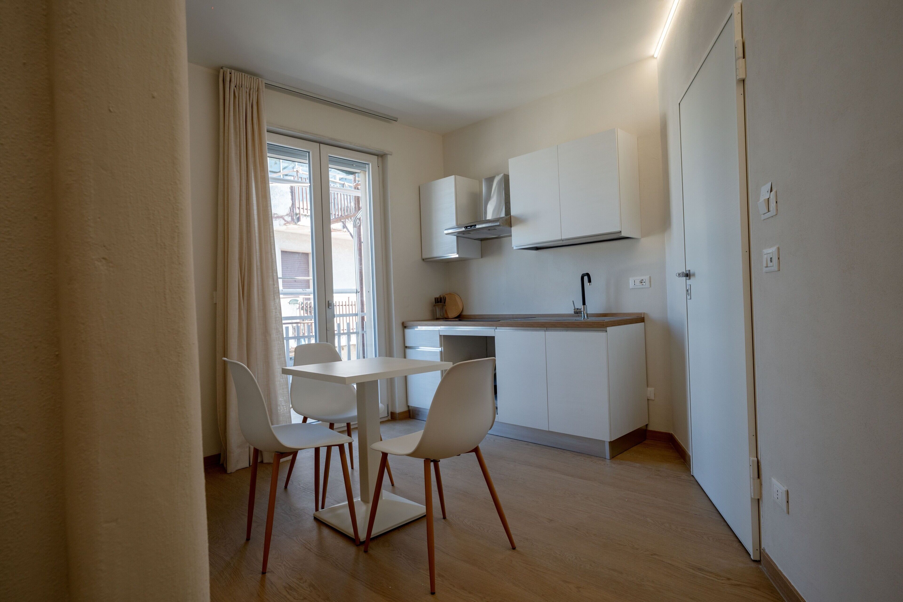 A compact kitchen with a dining area, white cabinets, and a window with curtains.
