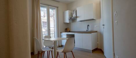 A compact kitchen with a dining area, white cabinets, and a window with curtains.