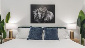 Ein Bett mit weißer Bettwäsche, zwei blaue Kissen und ein Gemälde von einem Schwarz-Weiß-Pferd darüber.