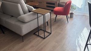 Ein Wohnzimmer mit einer Couch, einem roten Sessel, einem Couchtisch, einem Fernseher und einem Fenster mit Vorhängen.
