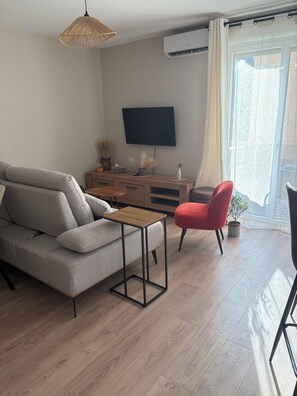 Ein Wohnzimmer mit einer Couch, einem roten Sessel, einem Couchtisch, einem Fernseher und einem Fenster mit Vorhängen.