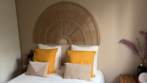 Ein Bett mit weißer Bettwäsche, zwei senfgelben Kissen und einem gewobenen Kopfteil.