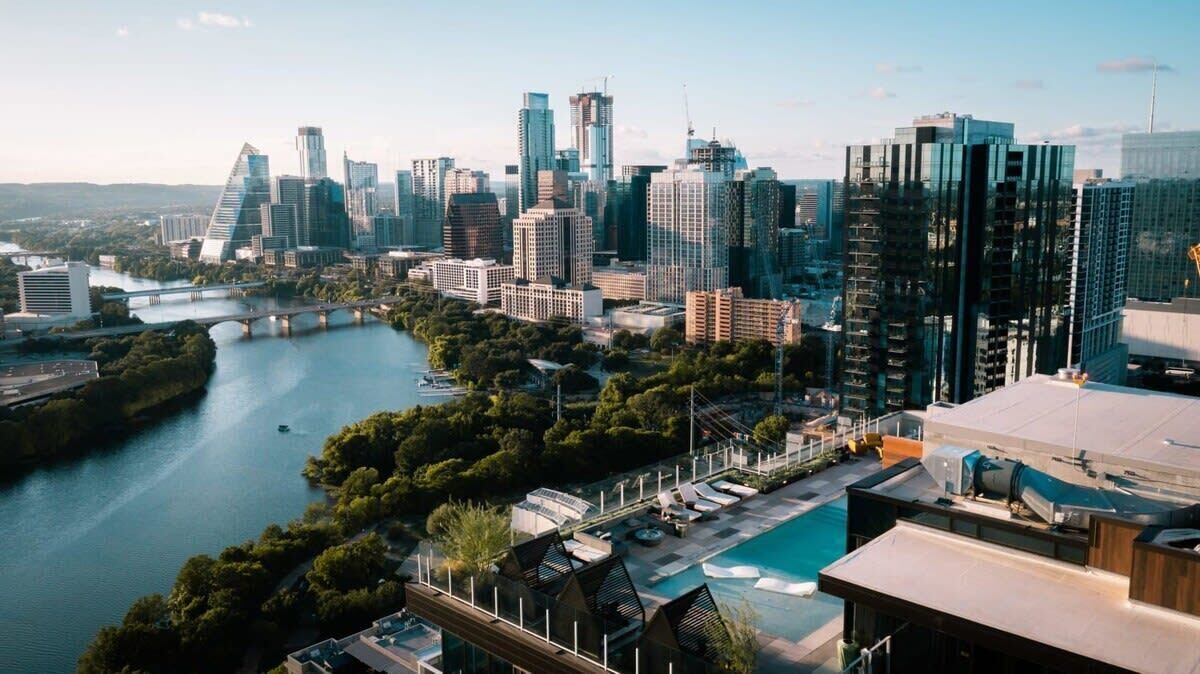 Un paisaje urbano moderno con rascacielos, un río y una zona de piscina en la azotea.