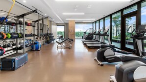 A modern gym with weightlifting equipment, treadmills, and a view of buildings through large windows. - Downtown Skyline & Lake Views l Rooftop Pool (Austin)