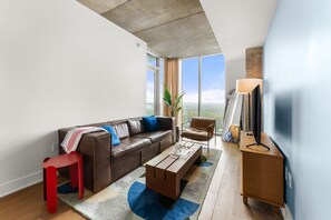 A modern living room with a leather sofa, a red chair, a coffee table, and a TV on a wooden stand. - Downtown Skyline & Lake Views l Rooftop Pool (Austin)
