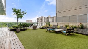 A rooftop garden with artificial grass, seating areas, and a view of surrounding buildings. - Downtown Skyline & Lake Views l Rooftop Pool (Austin)