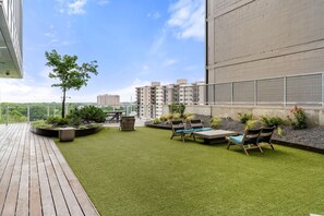 Jardim no terraço com grama artificial, áreas de estar e vista para edifícios próximos.
