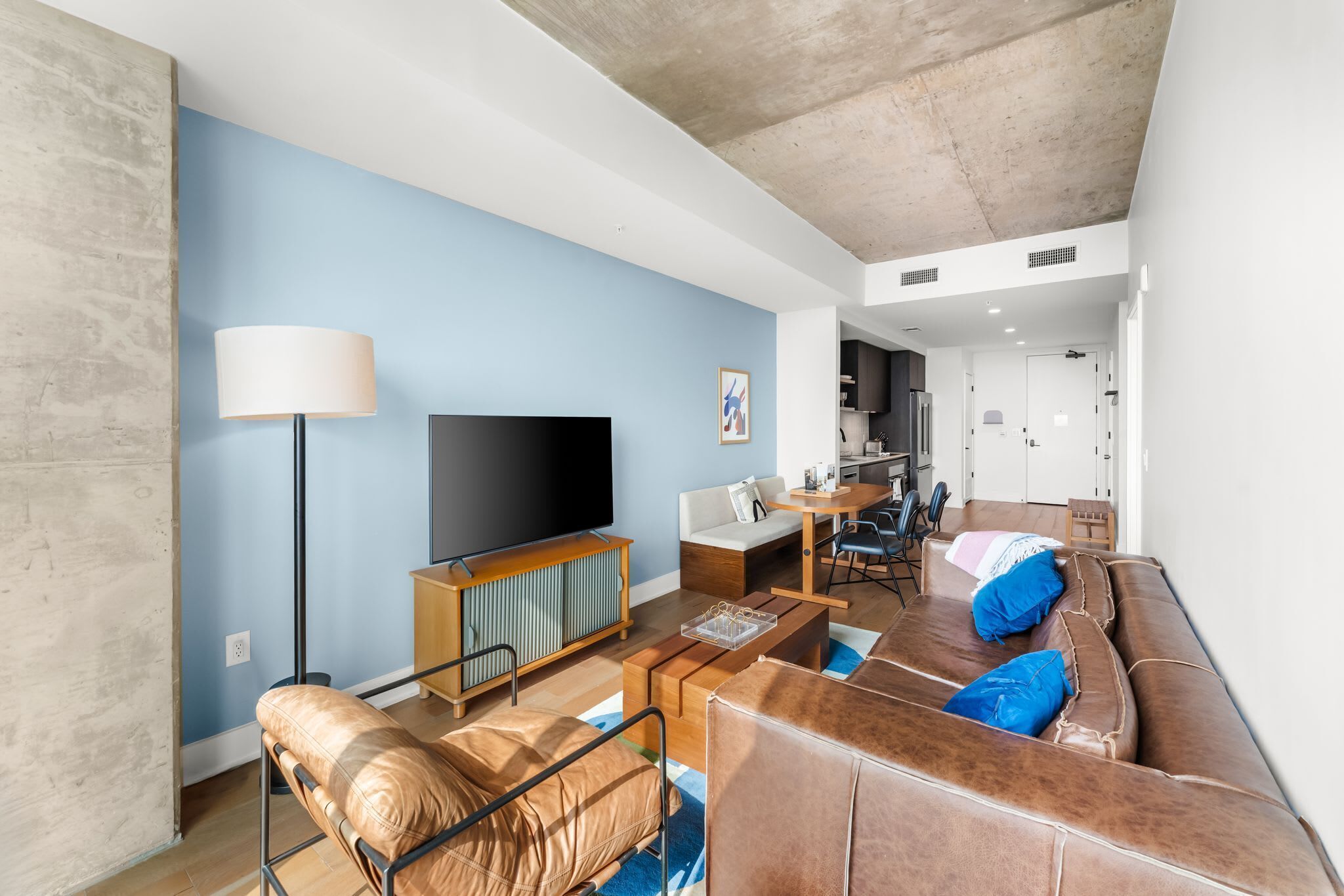 Ein modernes Wohnzimmer mit Flachbildfernseher, Sofa, Couchtisch und einem Essbereich mit Küche im Hintergrund.