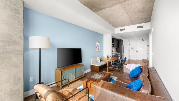 A modern living room with a flat-screen TV, sofa, coffee table, and a dining area with a kitchen in the background. - Downtown Skyline & Lake Views l Rooftop Pool (Austin)