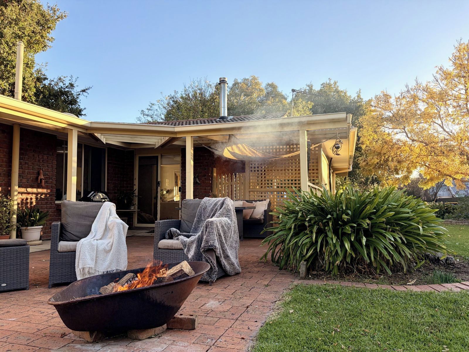 A covered outdoor seating area with a fire pit, wicker furniture, and a brick patio.
