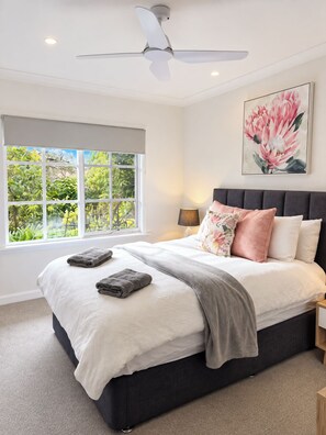 A bedroom with a bed, a ceiling fan, a window with a view of greenery, and a painting on the wall. - Hahndorf Creek Retreat 2 Bedroom (Hahndorf)
