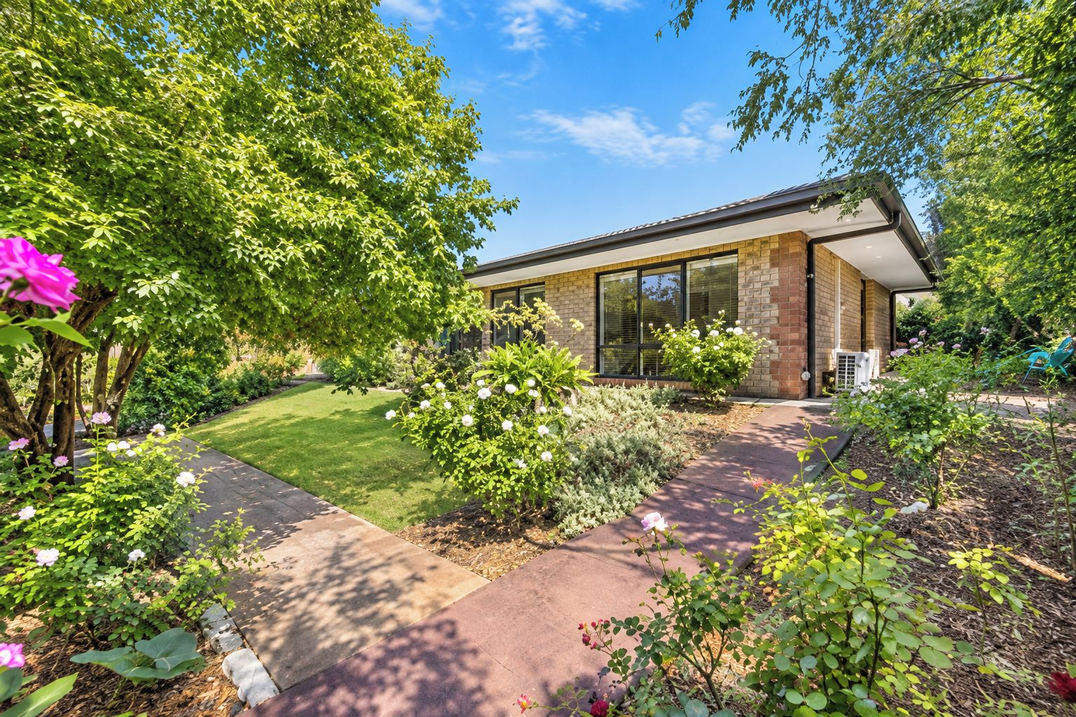 A modern house with a well-maintained garden, a paved driveway, and a large window overlooking the greenery.