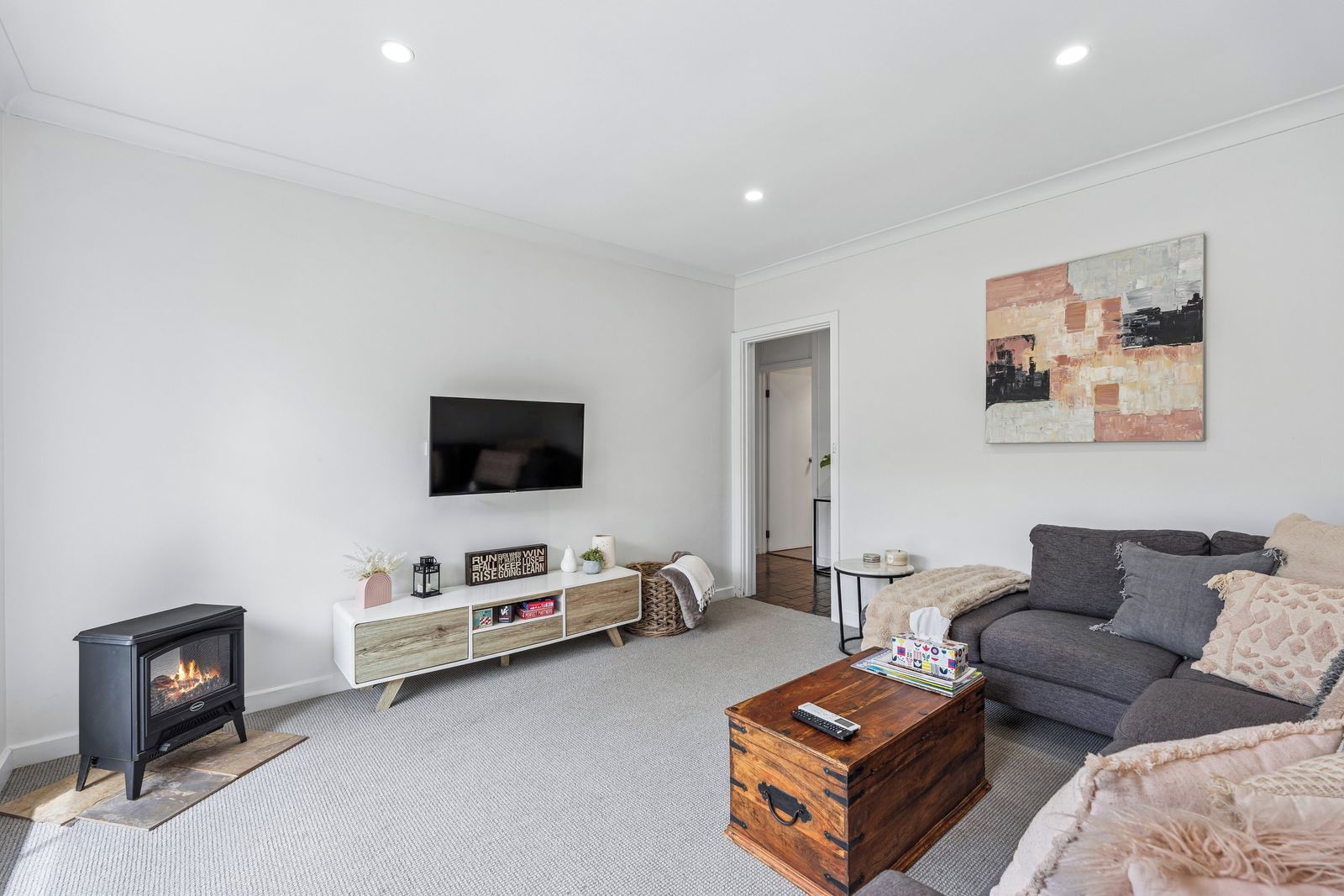 A modern living room with a fireplace, a flat-screen TV, a grey sofa, and a wooden coffee table.