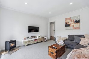A modern living room with a fireplace, a flat-screen TV, a grey sofa, and a wooden coffee table. - Hahndorf Creek Retreat 2 Bedroom (Hahndorf)